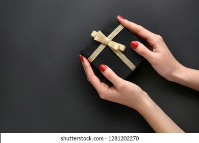 Female hands with manicure holding gift box on dark background