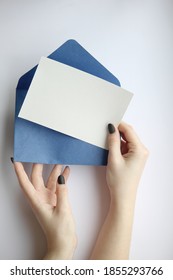 female hands with manicure holding a white sheet and a blue open envelope horizontally on a brown and white background.  postcard layout