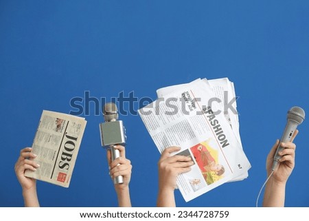 Female hands with microphones and newspapers on blue background