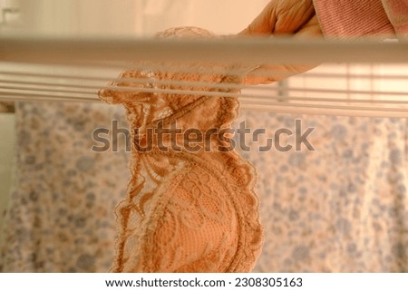 female hands of middle-aged woman close-up hang wet washed linen, bra on wire dryer, gentle hand washing of lacy underwear, housewife at homework, selective focus at shallow depth of field
