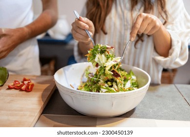 Female hands mixing green salad in the bowl with forks