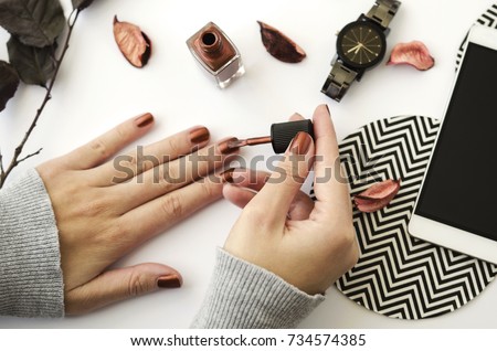 Female hands with nail polish on white background with mobile phone, watch and autumn petals.