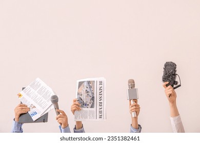 Female hands with newspapers and microphones on light background