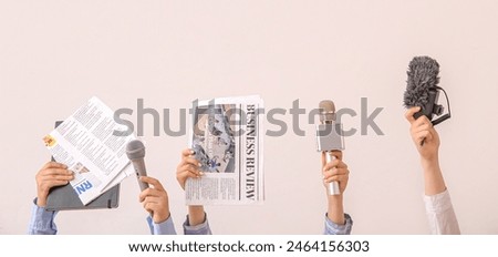 Female hands with newspapers and microphones on light background