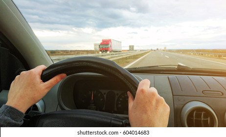 Female Hands On Car Steering Wheel Driving Vehicle On Two Lane Highway, Drivers Pov