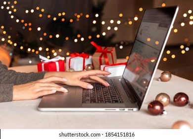 Female hands on the laptop with gifts and blurred bokeh lights. Christmas shopping online, sales and discounts promotions during winter holidays, online shopping at home and lockdown coronavirus