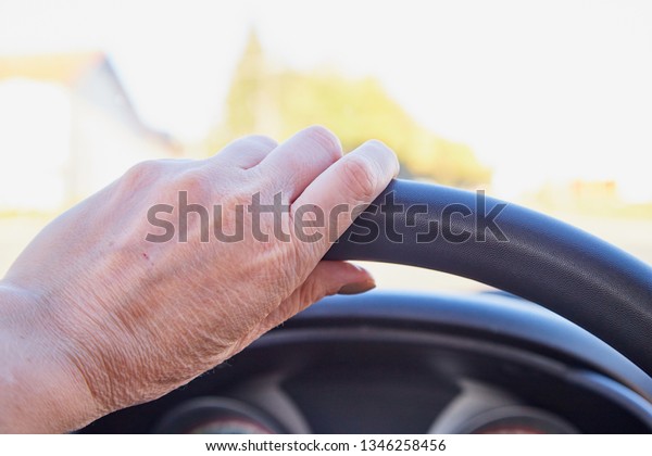 Female hands on\
the steering wheel of a car while driving and road background in an\
summer or an autumn day