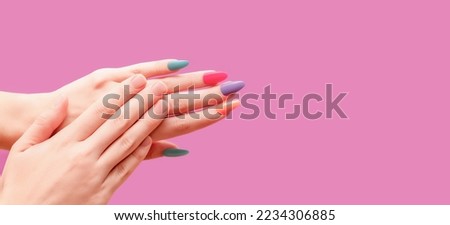 Female hands: one with colorful nail design and other without nail polish. Glitter nail polish manicure: purple, green, pink, and orange. Female model hands with perfect varicolored manicure on pink b