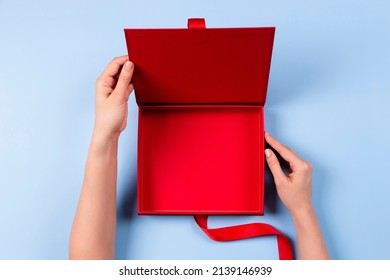 Female Hands Opening Empty Red Elegant Luxury Box With Ribbon. Mockup Present Gift Box On Light Blue Background. Top View