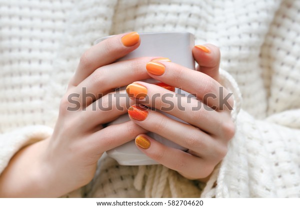 Female\
hands with orange nail design holding white\
cup.