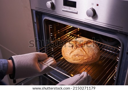 female hands in oven mitts take round bread out of the oven