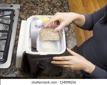 Female Hands Packing Lunch Into Portable Bag While In The Kitchen On Stone Counter Top Next To Stove