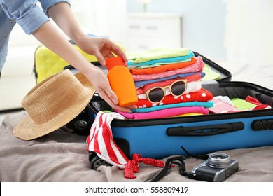 Female hands packing traveler case on bed, closeup