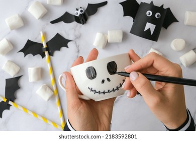 Female hands paint on white cup scary jacks face DIY for kids Halloween home activities Holiday art children craft Handmade decorations. Step by step Socially distanced at home Idea for art class