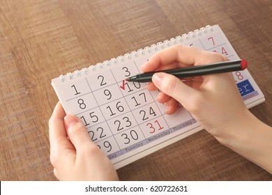 Female Hands Painting Check Mark In Calendar On Wooden Background