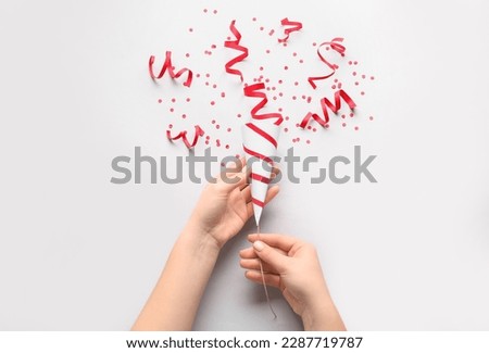 Female hands with party popper and confetti on light background