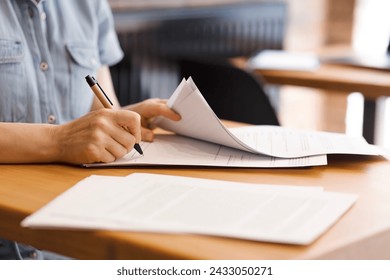 Female hands with pen signing documents, business papers on wooden table. Sign documents, loans, rent, work contracts, woman working in office, accountant, bank employee