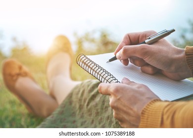 female hands with pen writing on notebook on grass outside - Shutterstock ID 1075389188