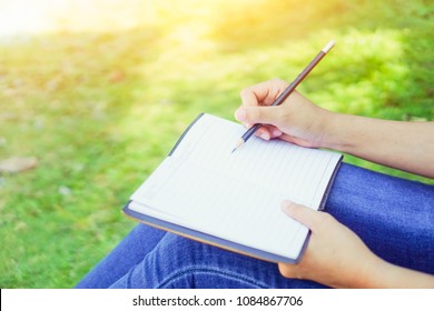 female hands with pen writing on notebook on grass outside - Shutterstock ID 1084867706