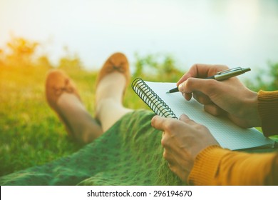 female hands with pen writing on notebook on grass outside