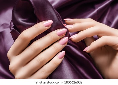 Female hands with pink nail design. Pink nail polish manicured hands. Woman hands hold purple fabric