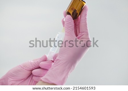 Female hands in a pink surgical  medical gloves holds a syringe and an ampoule. Hands in latex gloves close-up. Treatment and health care. Beauty injections and beauty treatments
