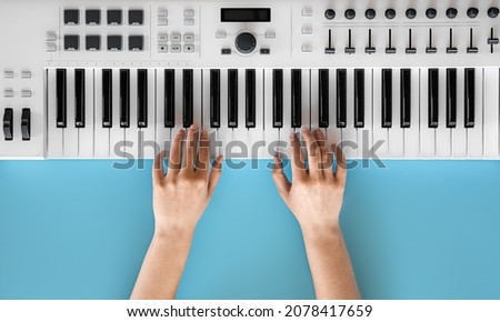 Female hands play musical keys on a blue background, top view.