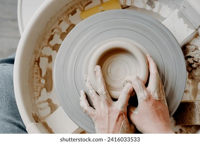 Female hands of a potter forming a clay product on a potter's wheel. Top view, close-up, abstract background for pottery making - Powered by Shutterstock