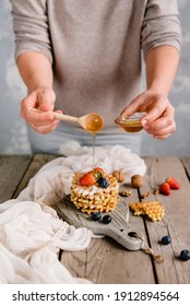 Female hands pour over a stack of waffles with honey and berries