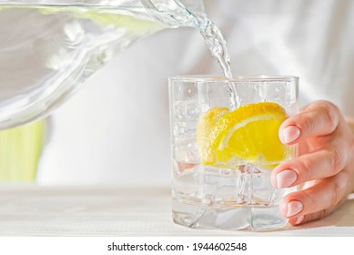 Female hands pouring water from the decanter into a glass beaker with lemon and ice. Health and diet concept. Quenching thirst on a hot day. - Powered by Shutterstock