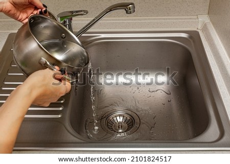 female hands pouring water from the pan into the sink in the kitchen. High quality photo