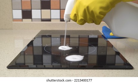 Female hands in protective gloves cleaning the surface of an induction cooker. - Shutterstock ID 2213400177