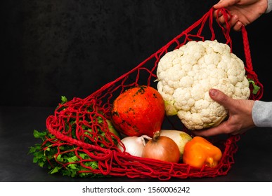 Female Hands Pull Vegetables From A Red String Bag After Shopping On A Black Background. Cauliflower Head In The Hand