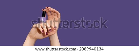 Female hands with purple nail design. Glitter purple nail polish manicure. Female hands hold purple nail polish on purple background. Copy space. Banner ad template. Advertising banner.