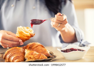 Weibliche Hände stecken Marmelade auf ein halbes Croissant am Morgen.