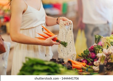 Female Hands Puts Fruits And Vegetables In Cotton Produce Bag At Food Market. Reusable Eco Bag For Shopping. Zero Waste Concept.