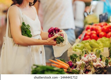 Female hands puts fruits and vegetables in cotton produce bag at food market. Reusable eco bag for shopping. Zero waste concept. - Shutterstock ID 1444441712