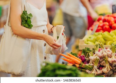 Female Hands Puts Fruits And Vegetables In Cotton Produce Bag At Food Market. Reusable Eco Bag For Shopping. Zero Waste Concept.