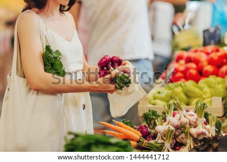 Female hands puts fruits and vegetables in cotton produce bag at food market. Reusable eco bag for shopping. Zero waste concept.