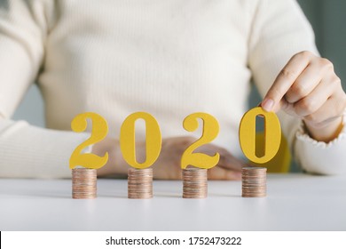 Female Hands Putting Gold Wooden Number 2020 On Stack Of Coins. Tax Payment, Investment And Banking.2020 New Year Saving Money And Financial Planning Concept. 