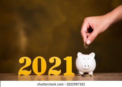 Female Hands Putting Gold Wooden Number 2021 On Stack Of Coins. Saving Money And Finance Concept.