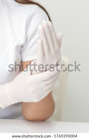 Female hands putting on protective white latex medical gloves during epidemic in quarantine