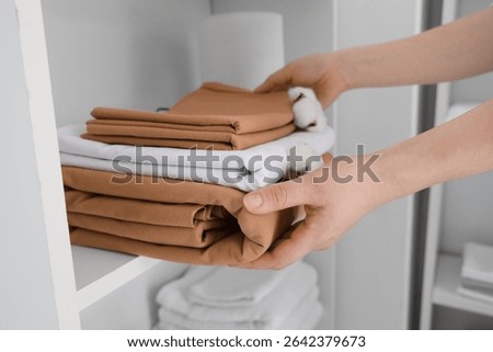 Female hands putting stack of clean bed sheets with cotton flowers on shelf at home, closeup