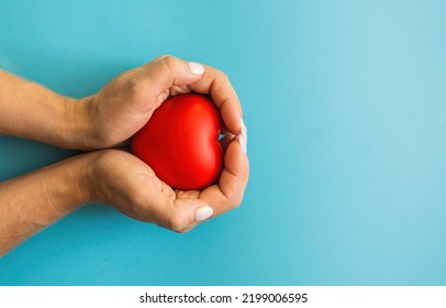 In Female Hands A Red Heart On A Blue Background, Copyspace On The Right. Women's Heart Health. Maternal Love And Care Concept. Mother's Good Heart