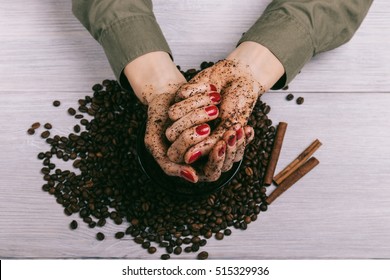 Female hands with red manicure with applied scrub over coffee beans, close-up