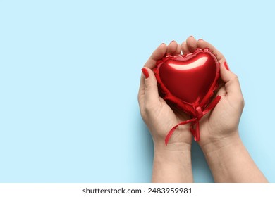 Female hands with red manicure and heart shaped balloon on blue background. Valentine's Day celebration - Powered by Shutterstock