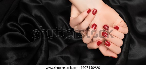 Female hands with\
red nail design. Red nail polish manicure. Woman hands on black\
fabric background. Copy\
space