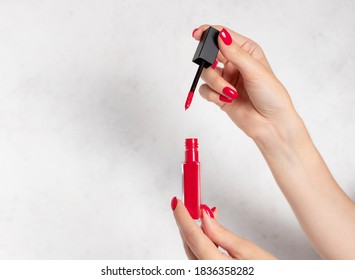 female hands with red nails opening red liquid lipstick. Fashion beauty makeup and cosmetics. white background with copy space