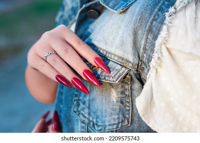 Female Hands With Red Stiletto Nail Design. Glitter Red Nail Polish Manicure. Female Model In Jeans Jacket With Red Stiletto Manicure.