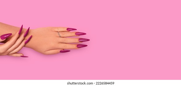 Female hands with red stiletto nail design. Glitter red nail polish manicure. Female hands with stiletto nails design on pink background. Copy space. Plce for text.